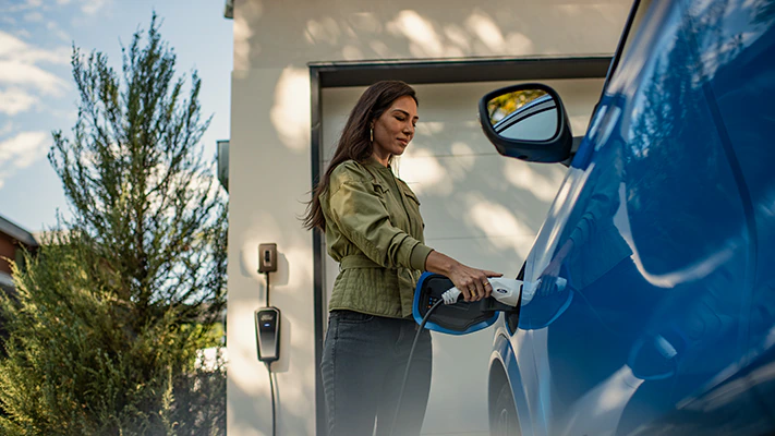 A driver plugging in the available Ford Accessory charging cable to a blue 2023 Ford Mustang Mach-E® SUV.
